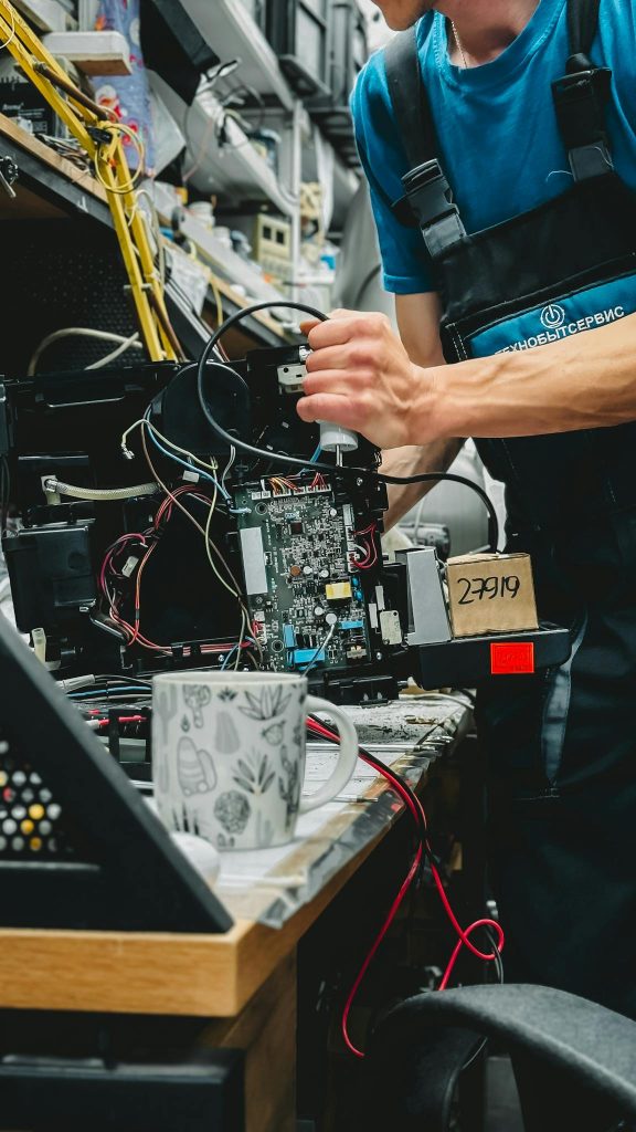 Technician working on printer repair with tools in a cluttered workshop environment.